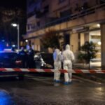 Esterno notturno di un palazzo residenziale a Roma con nastro della polizia e agenti sullo sfondo.