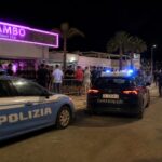 Esterno notturno di una discoteca sul litorale calabrese con pattuglie e luci di emergenza.