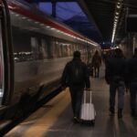 Agenti di polizia in una stazione ferroviaria di Milano vicino a un treno, in una scena di cronaca sobria.