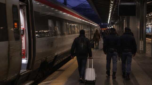 Agenti di polizia in una stazione ferroviaria di Milano vicino a un treno, in una scena di cronaca sobria.