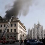 Incendio sul tetto di un palazzo a Milano con fumo nero visibile dal Duomo e vigili del fuoco sul posto.