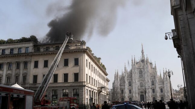 Incendio sul tetto di un palazzo a Milano con fumo nero visibile dal Duomo e vigili del fuoco sul posto.
